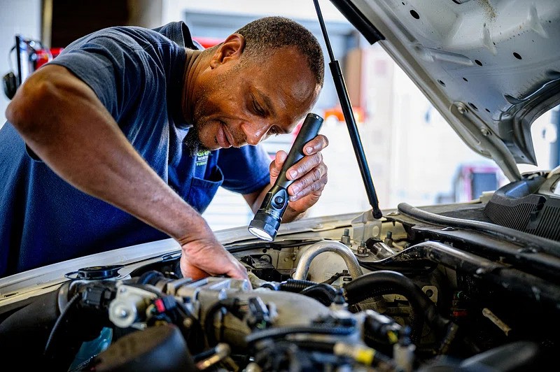 mechanic inspecting car engine bay with torch car maintenance